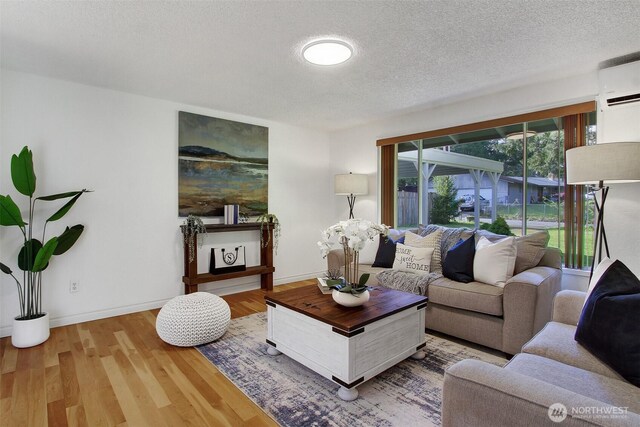 living room featuring baseboards, a textured ceiling, a wall unit AC, and wood finished floors