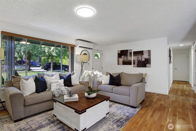 living room featuring wood finished floors, baseboards, a textured ceiling, and a wall mounted AC