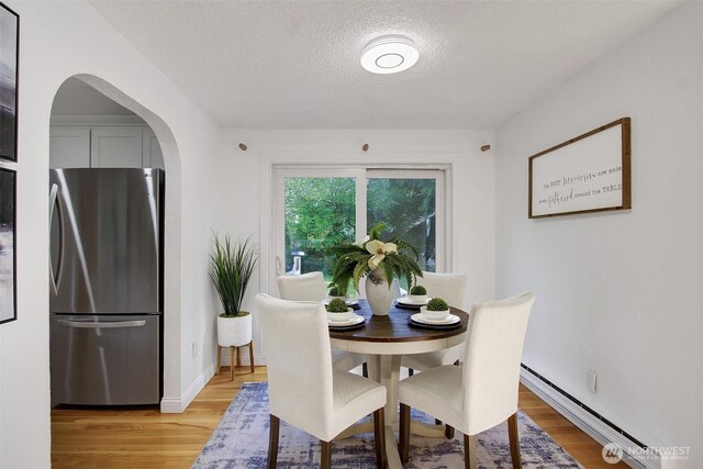 dining space featuring arched walkways, light wood finished floors, a textured ceiling, and baseboard heating