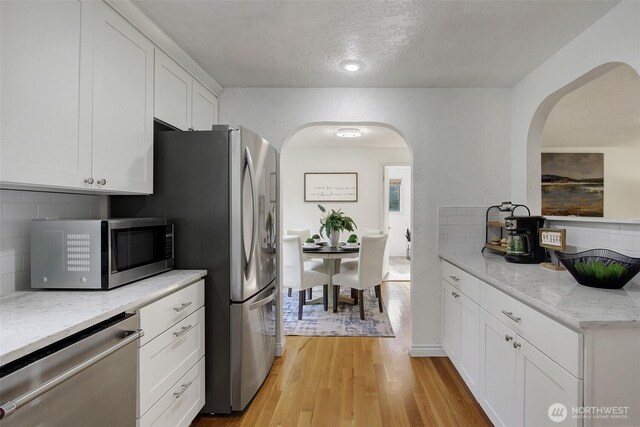 kitchen with light wood-style floors, appliances with stainless steel finishes, arched walkways, and white cabinetry