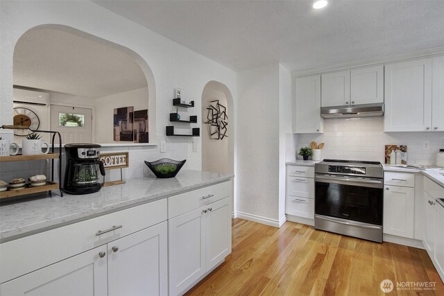 kitchen with stainless steel electric range, a wall mounted air conditioner, backsplash, white cabinetry, and under cabinet range hood