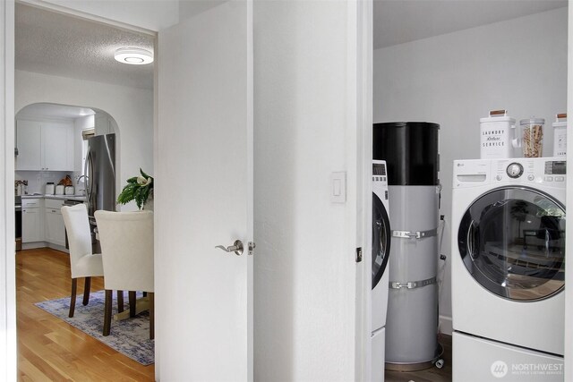 clothes washing area featuring laundry area, independent washer and dryer, arched walkways, light wood finished floors, and secured water heater