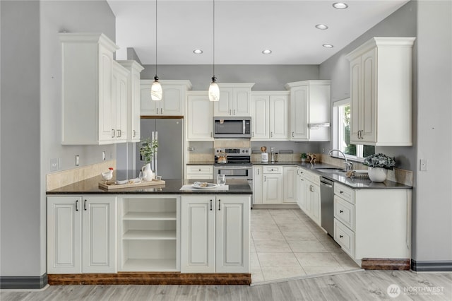 kitchen featuring dark countertops, appliances with stainless steel finishes, a sink, a peninsula, and white cabinetry