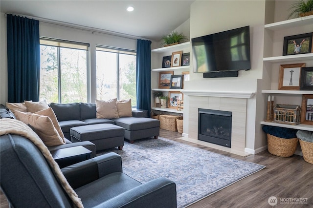 living room with vaulted ceiling, a tile fireplace, built in shelves, wood finished floors, and recessed lighting