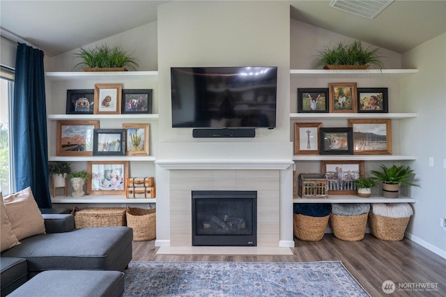 living area with visible vents, lofted ceiling, a tile fireplace, and wood finished floors