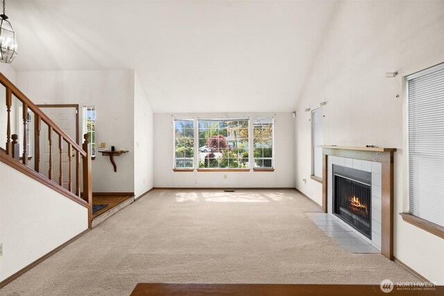 unfurnished living room featuring a tiled fireplace, stairway, carpet, and vaulted ceiling