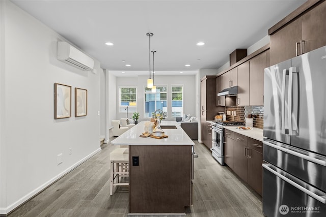 kitchen featuring light countertops, under cabinet range hood, a wall mounted AC, a sink, and stainless steel appliances