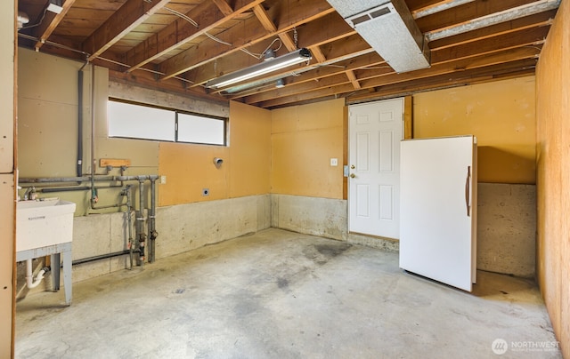 basement with freestanding refrigerator and a sink
