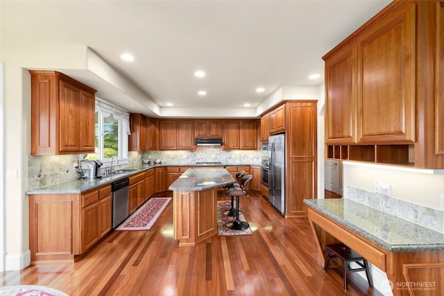 kitchen with brown cabinets, stainless steel appliances, a sink, and light wood-style flooring