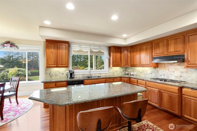 kitchen with a sink, dark wood finished floors, a wealth of natural light, stainless steel gas stovetop, and under cabinet range hood