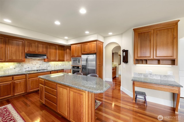 kitchen with under cabinet range hood, arched walkways, appliances with stainless steel finishes, and dark wood-type flooring