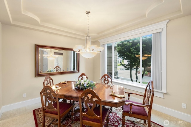 dining space featuring carpet floors, a raised ceiling, baseboards, and a notable chandelier