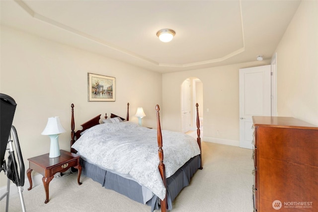 bedroom featuring a raised ceiling, baseboards, light carpet, and arched walkways