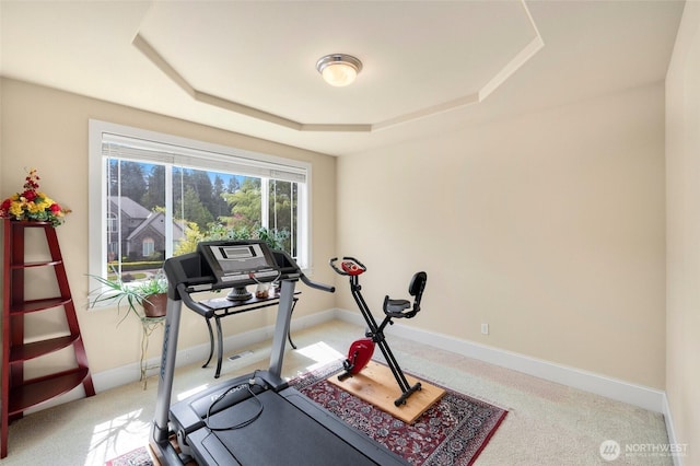 exercise area featuring baseboards, light carpet, and a tray ceiling
