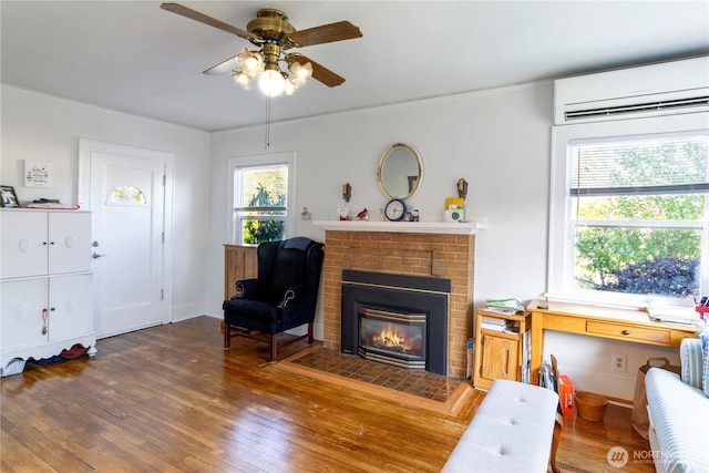 sitting room featuring a fireplace, ceiling fan, wood-type flooring, and an AC wall unit