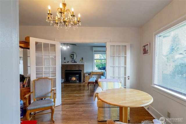 dining area with wood finished floors, a fireplace, baseboards, a wall unit AC, and ceiling fan with notable chandelier