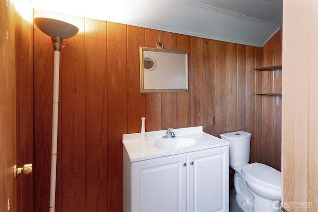 bathroom featuring toilet, wood walls, and vanity