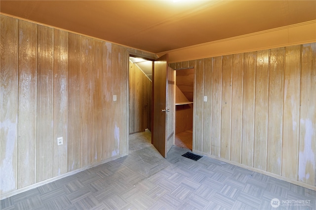 unfurnished room with baseboards, wood walls, and visible vents