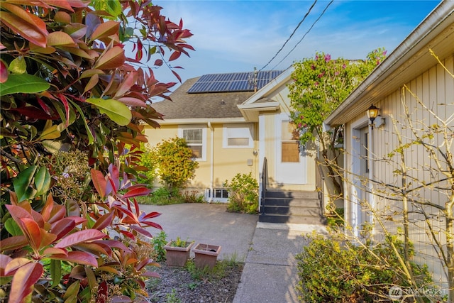 doorway to property featuring roof mounted solar panels and roof with shingles