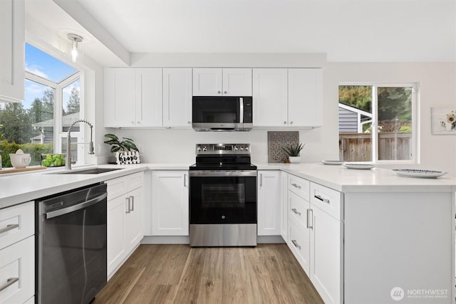kitchen with a peninsula, light countertops, white cabinets, a sink, and appliances with stainless steel finishes