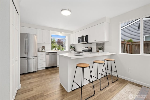 kitchen featuring a kitchen breakfast bar, appliances with stainless steel finishes, light wood-type flooring, white cabinets, and a peninsula