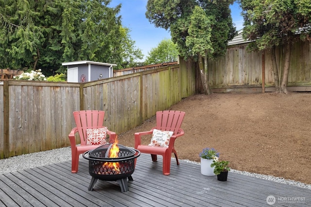 deck featuring a fenced backyard, an outdoor fire pit, and a storage shed