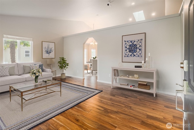 living area with arched walkways, baseboards, wood finished floors, and vaulted ceiling with skylight