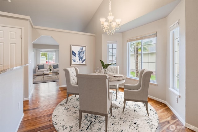 dining area featuring light wood-style floors, baseboards, a chandelier, arched walkways, and vaulted ceiling
