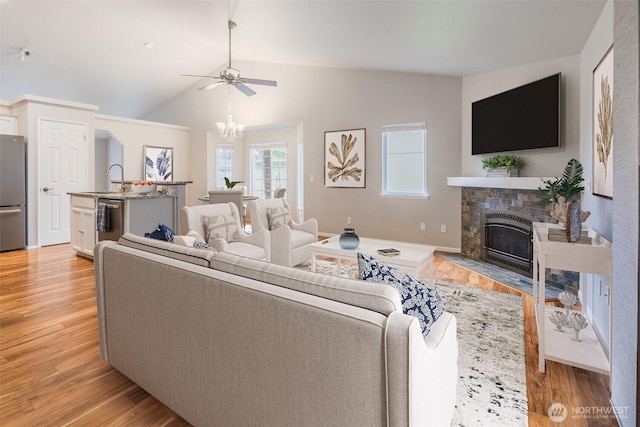living room featuring vaulted ceiling, a fireplace with flush hearth, ceiling fan with notable chandelier, and light wood-style floors