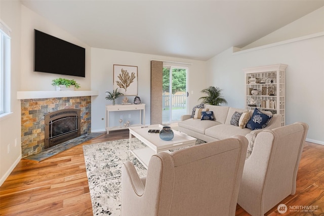 living area featuring a fireplace with flush hearth, baseboards, wood finished floors, and lofted ceiling