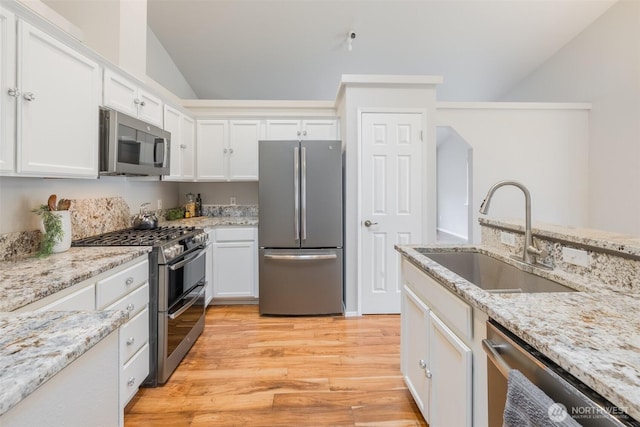 kitchen featuring white cabinets, a sink, light wood-style flooring, vaulted ceiling, and stainless steel appliances
