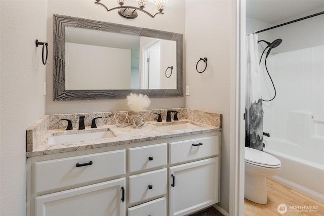 bathroom featuring double vanity, toilet, a sink, and wood finished floors