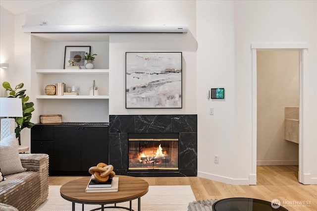 living area with built in features, baseboards, light wood-style flooring, and a premium fireplace