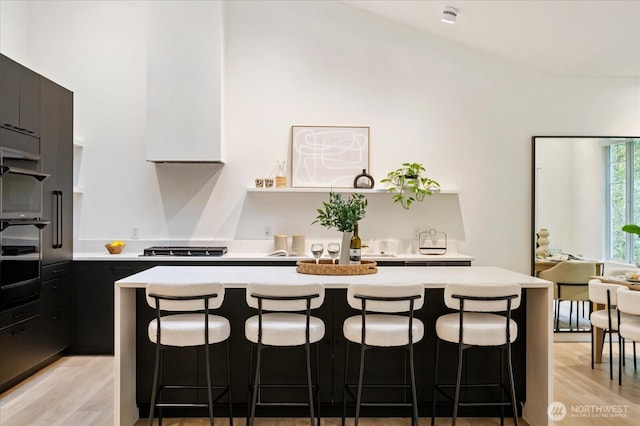 kitchen with light countertops, wall oven, a breakfast bar, and light wood finished floors