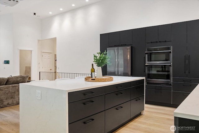 kitchen with dark cabinetry, freestanding refrigerator, a high ceiling, and light countertops
