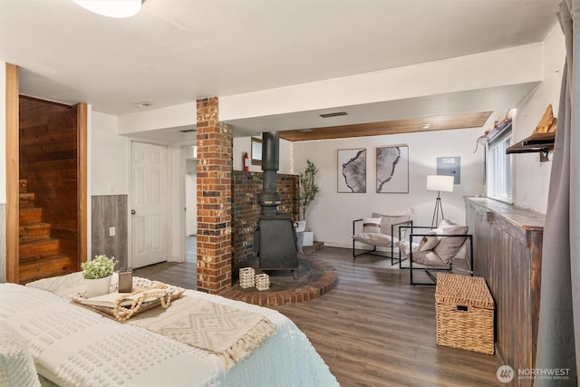 bedroom with a wood stove, dark wood-style floors, and visible vents
