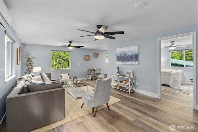 living area featuring wood finished floors, a ceiling fan, a wall unit AC, and baseboard heating