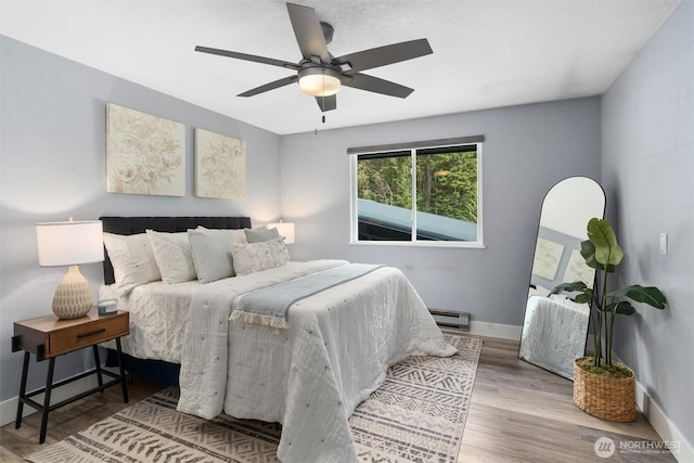 bedroom featuring baseboards, a ceiling fan, a baseboard heating unit, and wood finished floors