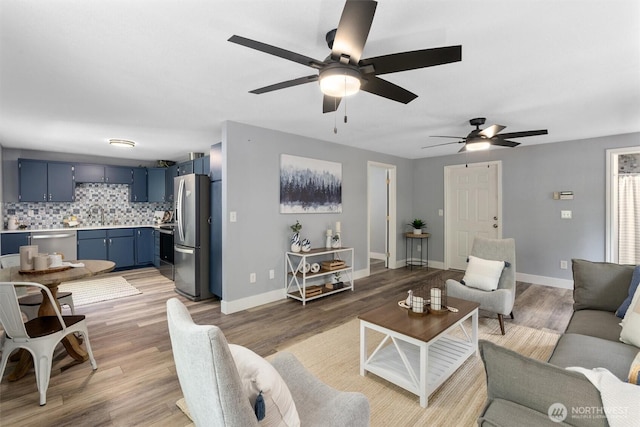 living room featuring light wood-type flooring, baseboards, and ceiling fan
