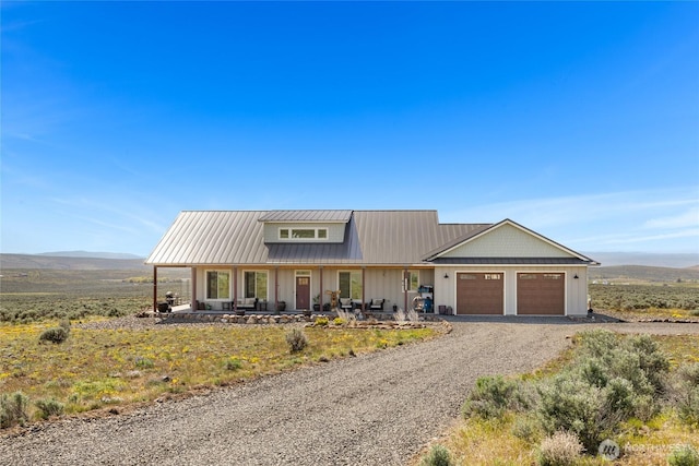 view of front of property with covered porch, driveway, metal roof, a mountain view, and an attached garage