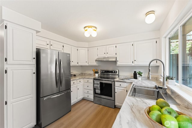 kitchen with a sink, light stone counters, under cabinet range hood, light wood-style floors, and stainless steel appliances