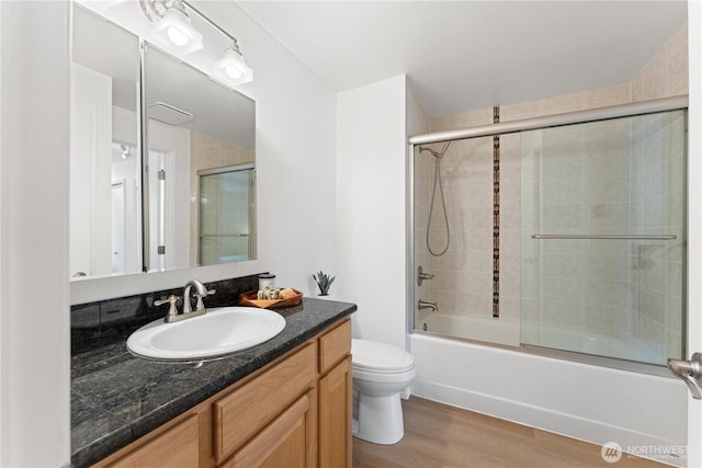 bathroom with vanity, bath / shower combo with glass door, wood finished floors, and toilet