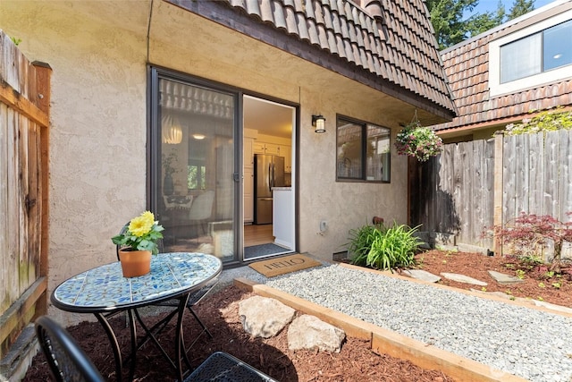 property entrance with stucco siding, a tiled roof, and fence