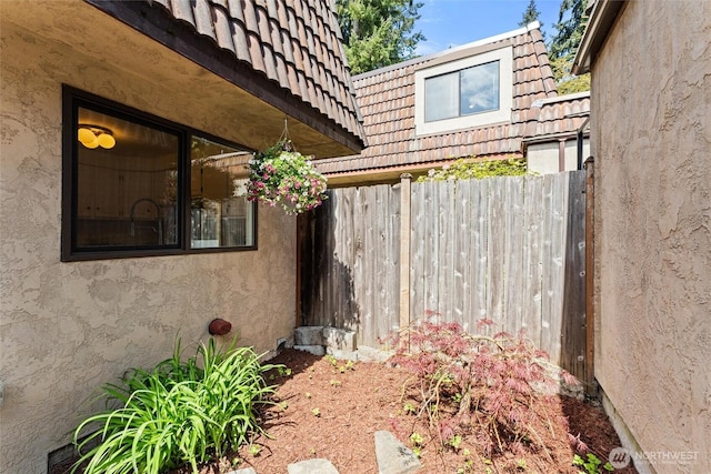 view of home's exterior with mansard roof, fence, a tile roof, and stucco siding