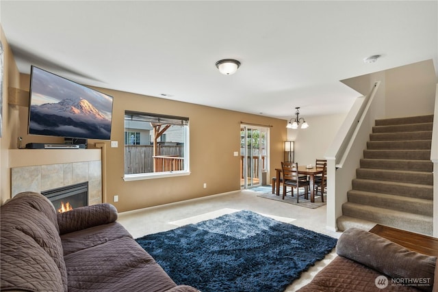living area featuring stairs, baseboards, a tile fireplace, carpet flooring, and a notable chandelier