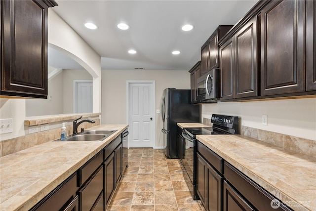 kitchen with dark brown cabinets, arched walkways, appliances with stainless steel finishes, and a sink