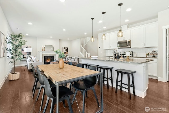 dining room with dark wood-style flooring, stairway, baseboards, a glass covered fireplace, and recessed lighting