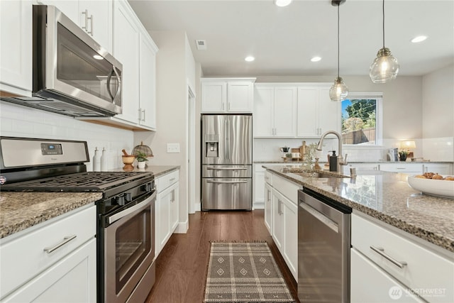 kitchen featuring white cabinets, light stone counters, a sink, stainless steel appliances, and decorative backsplash