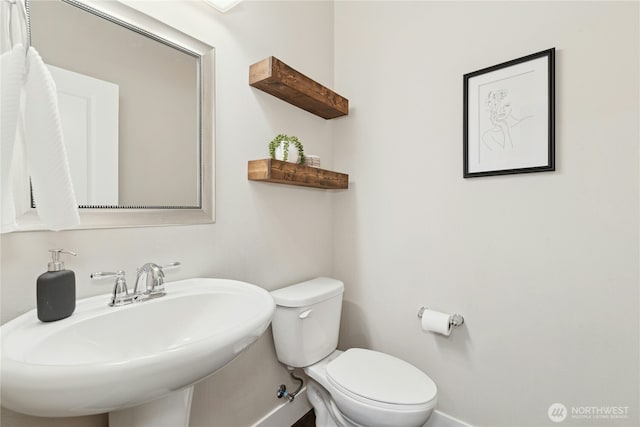 half bath with toilet, baseboards, and a sink