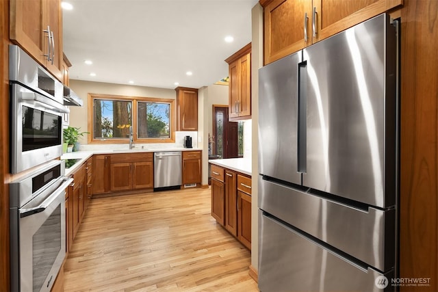 kitchen with appliances with stainless steel finishes, a sink, light countertops, brown cabinetry, and light wood-type flooring